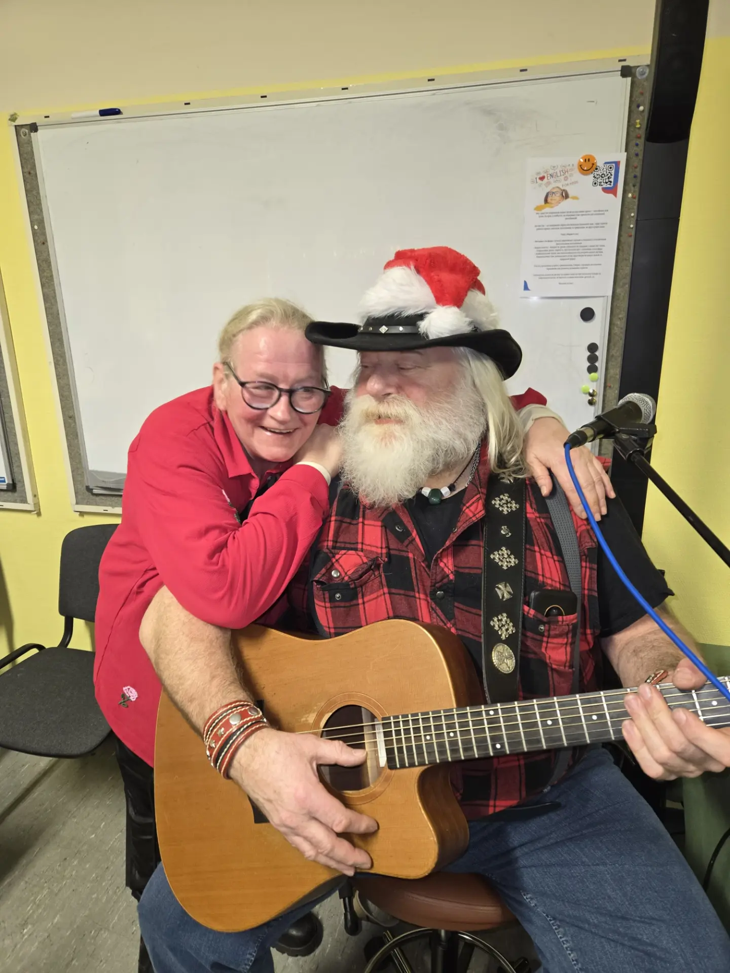 Zwei Personen umarmen sich, einer mit Gitarre und Weihnachtsmütze