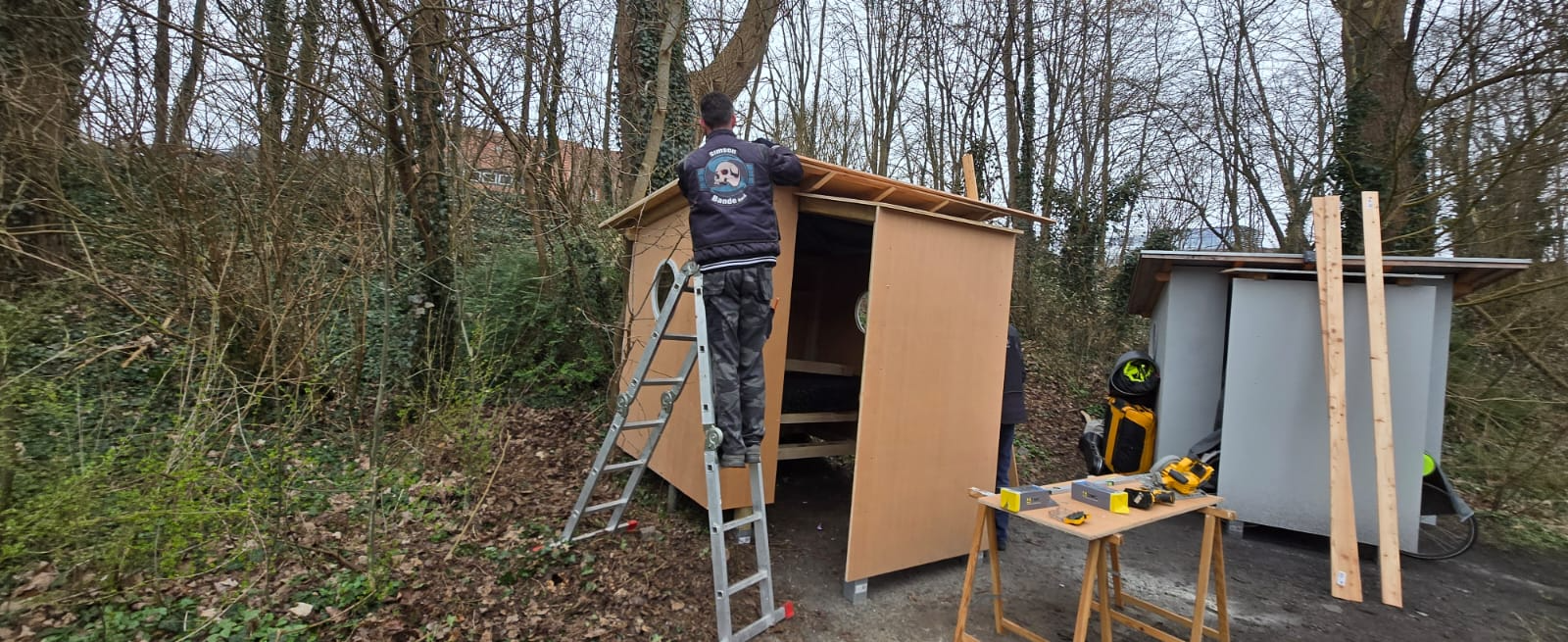Helfer auf Leiter montiert die Wandplatten der Holzhütte